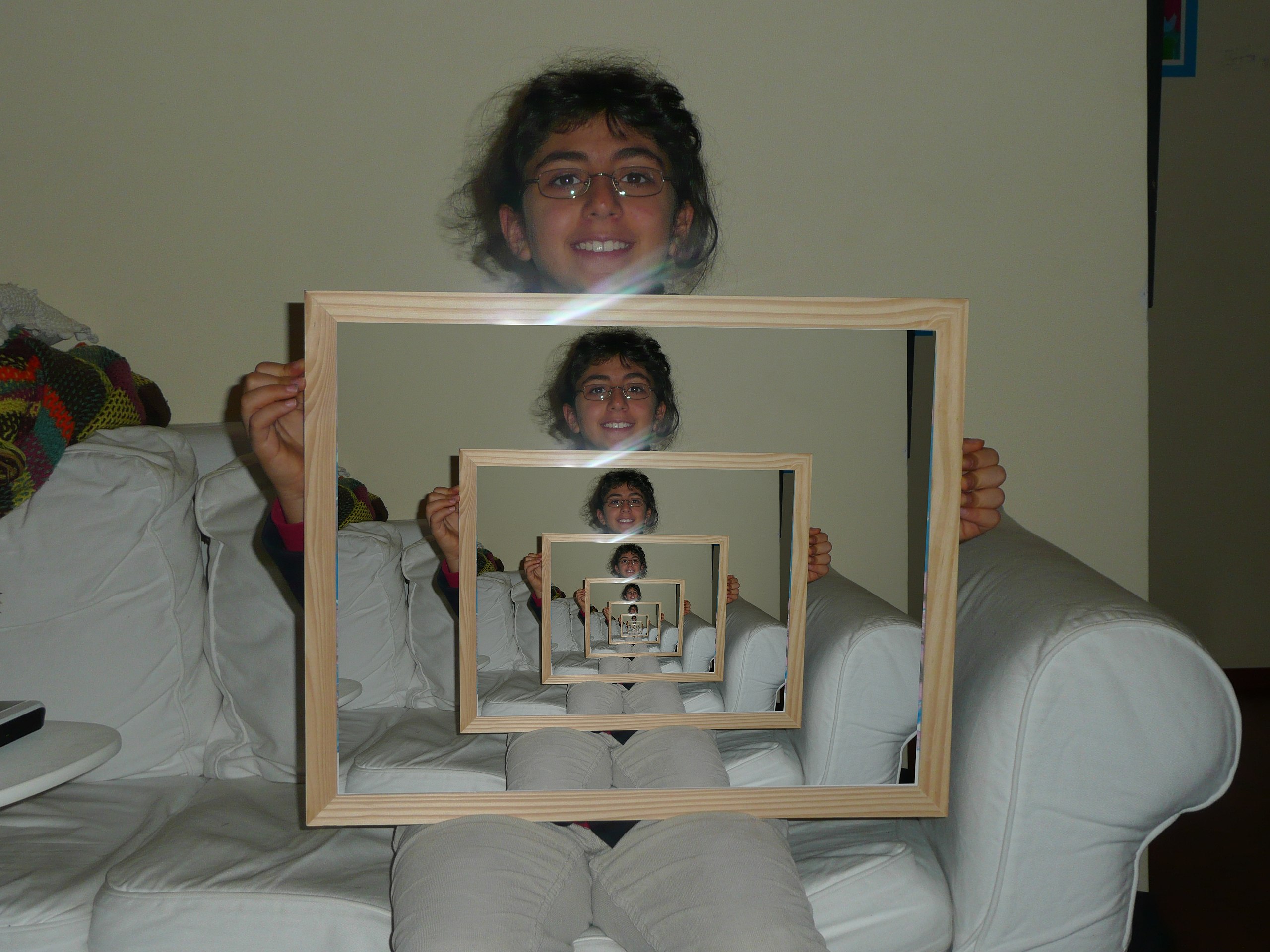 A lady holding a picture frame. Inside the frame, there is the image of the same lady holding the picture frame. It recursively repeat itself